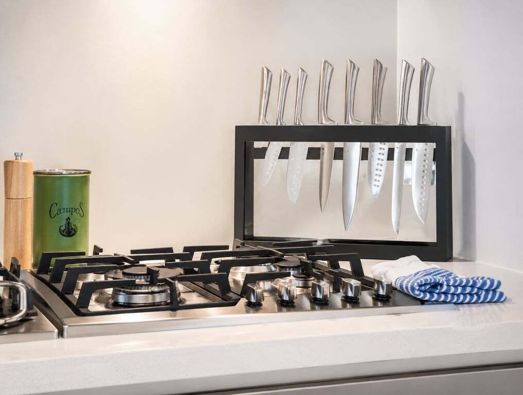 Una cocina con estufa a gas, un colgador de cuchillos, una lata de CampoS y una toalla azul y blanca.