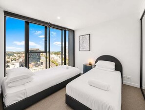 A hotel room with two beds, large windows, a city view, a framed map on the wall, and a nightstand with a lamp. - 2BR Stay in Fortitude Valley w/ pool and gym (Brisbane)