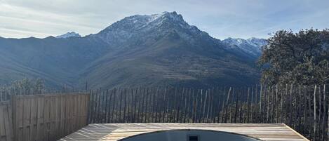 Un jacuzzi con vistas a la montaña, rodeado por una terraza de madera y una valla de madera.