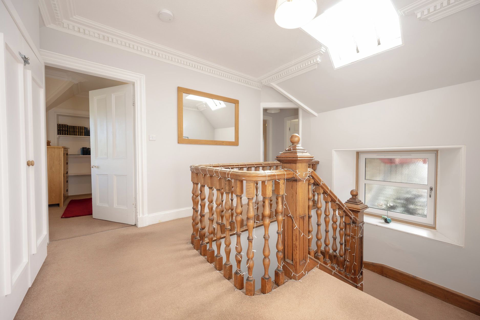 A hallway with a wooden staircase, a mirror, and a window with a view.