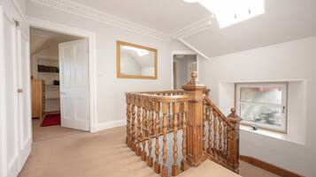 A hallway with a wooden staircase, a mirror, and a window with a view.