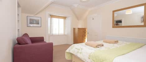 A bedroom with a bed, a chair, a wardrobe, a window, and a mirror.