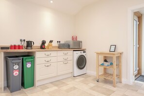 Cocina compacta con lavadora, cafetera y contenedores para reciclaje.