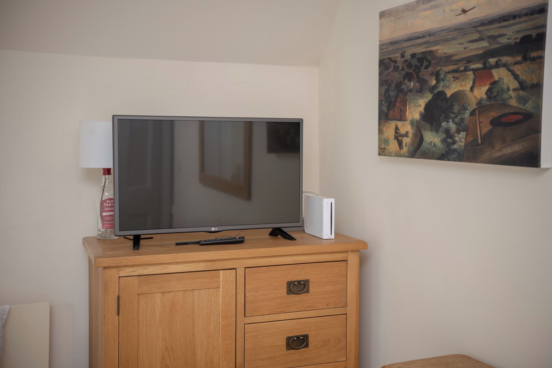 Un televisor sobre un mueble de madera con un control remoto, una lámpara y un cuadro en la pared.