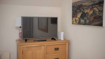Un televisor sobre un mueble de madera con un control remoto, una lámpara y un cuadro en la pared.