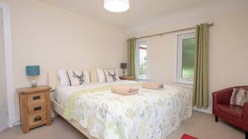 Un dormitorio con una cama, mesitas de noche, una silla roja y una ventana con cortinas.