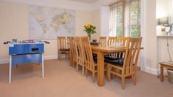 Un área de comedor con una mesa y sillas de madera, una mesa de fútbol de mesa, un mapa mundial en la pared y una ventana con persianas.