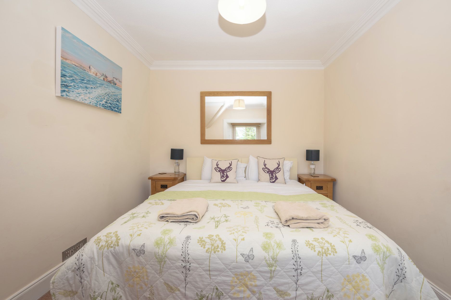 A bedroom with a bed, two bedside tables, a nightstand, a mirror, and a painting on the wall.