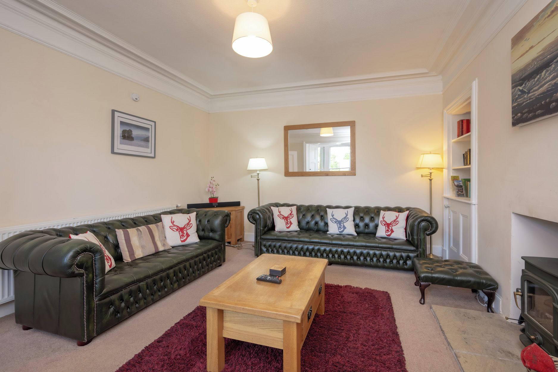 A living room with two green leather sofas, a wooden coffee table, and a red rug.