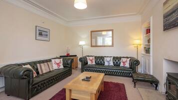 A living room with two green leather sofas, a wooden coffee table, and a red rug.