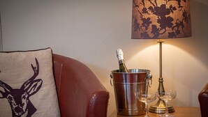 Ein Ledersofa mit einem Hirschkissen, ein Champagnerkübel aus Metall mit einer Flasche, zwei Weingläser und eine Lampe auf einem Holztisch.