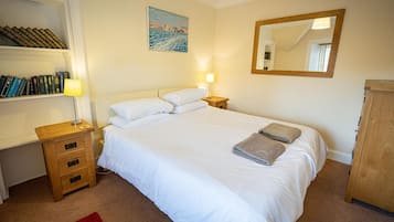 A neatly arranged bedroom with a bed, bedside tables, a bookshelf, a painting, and a mirror.