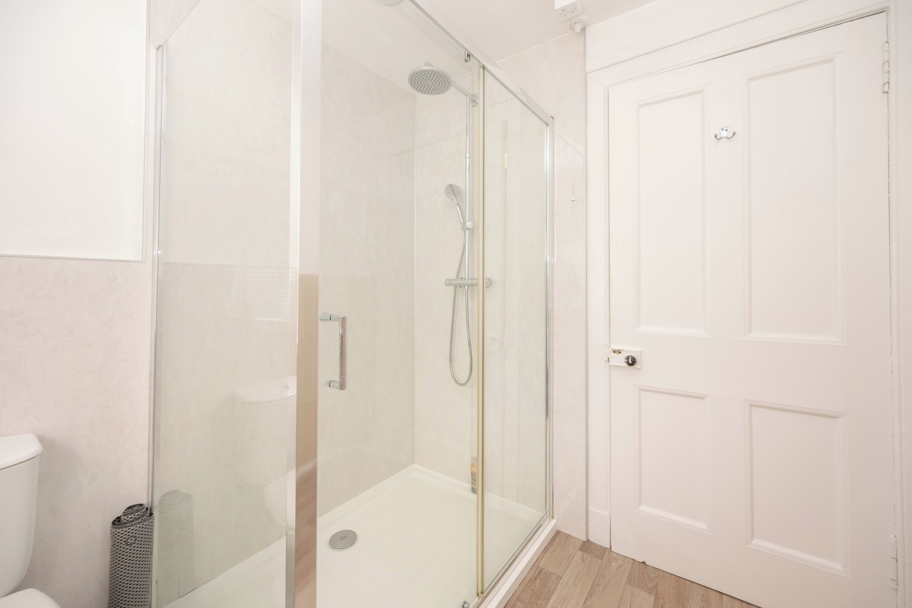 Un baño con ducha de vidrio, inodoro y puerta blanca.