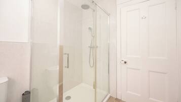 Un baño con ducha de vidrio, inodoro y puerta blanca.
