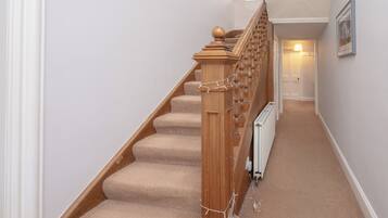Una escalera alfombrada con barandillas de madera y pasamanos, que conduce a una habitación con radiador y puerta.