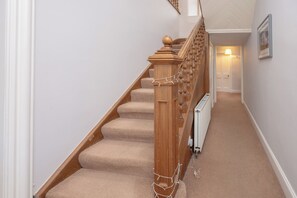 Una escalera alfombrada con barandillas de madera y pasamanos, que conduce a una habitación con radiador y puerta.