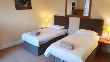 A hotel room with two beds, a mirror, a painting, and a red rug.