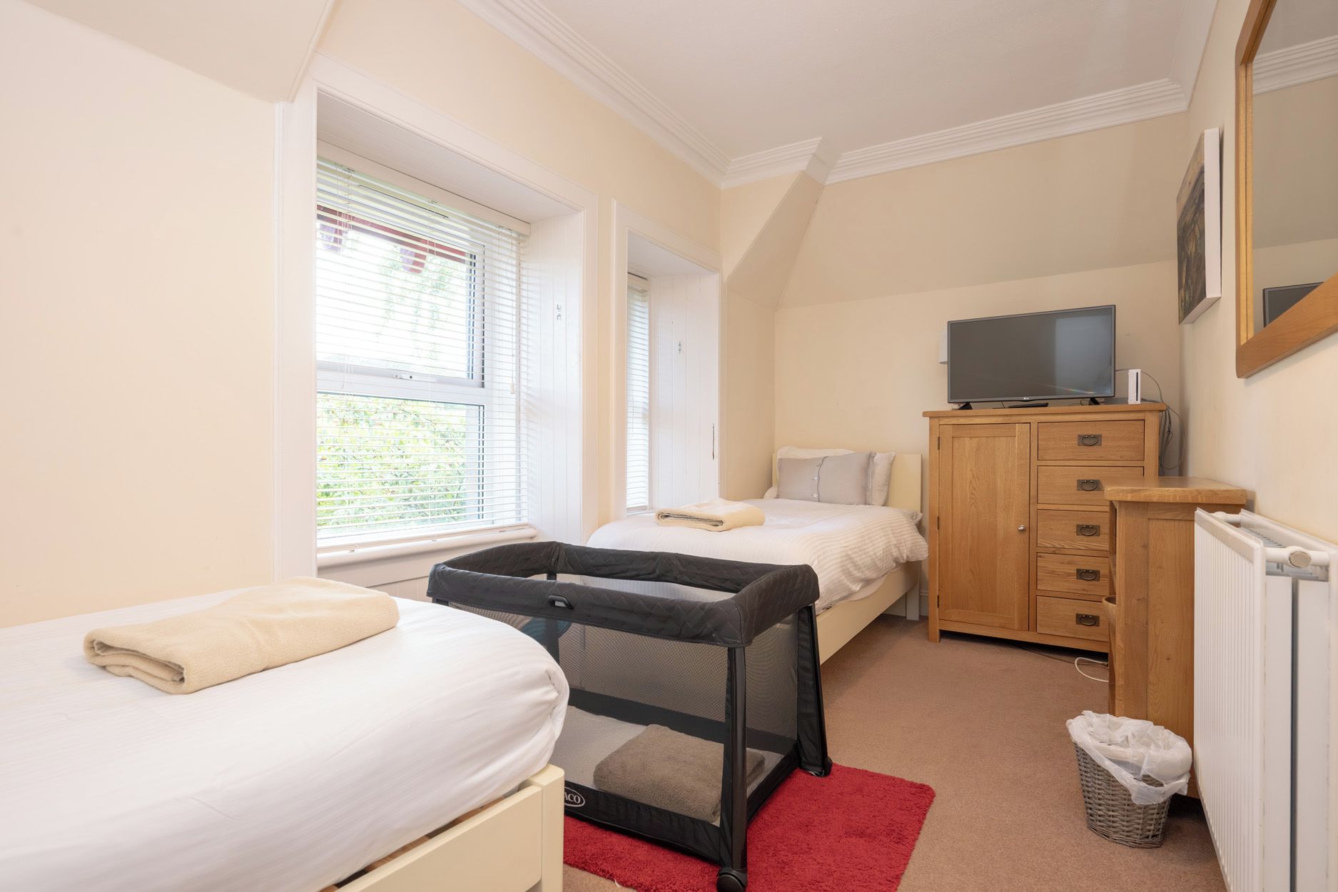 A bedroom with a bed, a small desk, a TV, and a window with blinds.