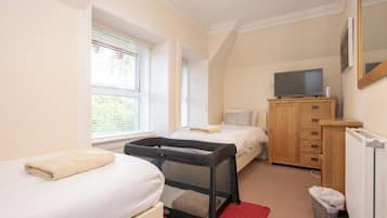 A bedroom with a bed, a small desk, a TV, and a window with blinds.