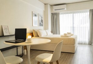 A modern hotel room with a bed, a desk with a laptop, a round table, and a chair. - Rent Up - San Telmo Amenities Premium (Buenos Aires)