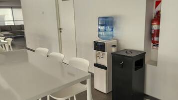 A conference room with a long table, white chairs, a water dispenser, a fire extinguisher, and a small trash bin.