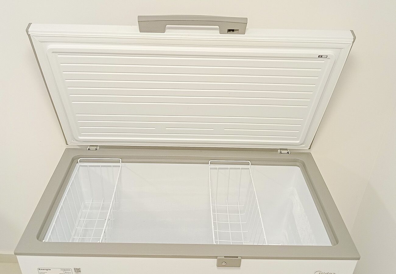 A white chest freezer with a handle on top and a grid shelf inside.