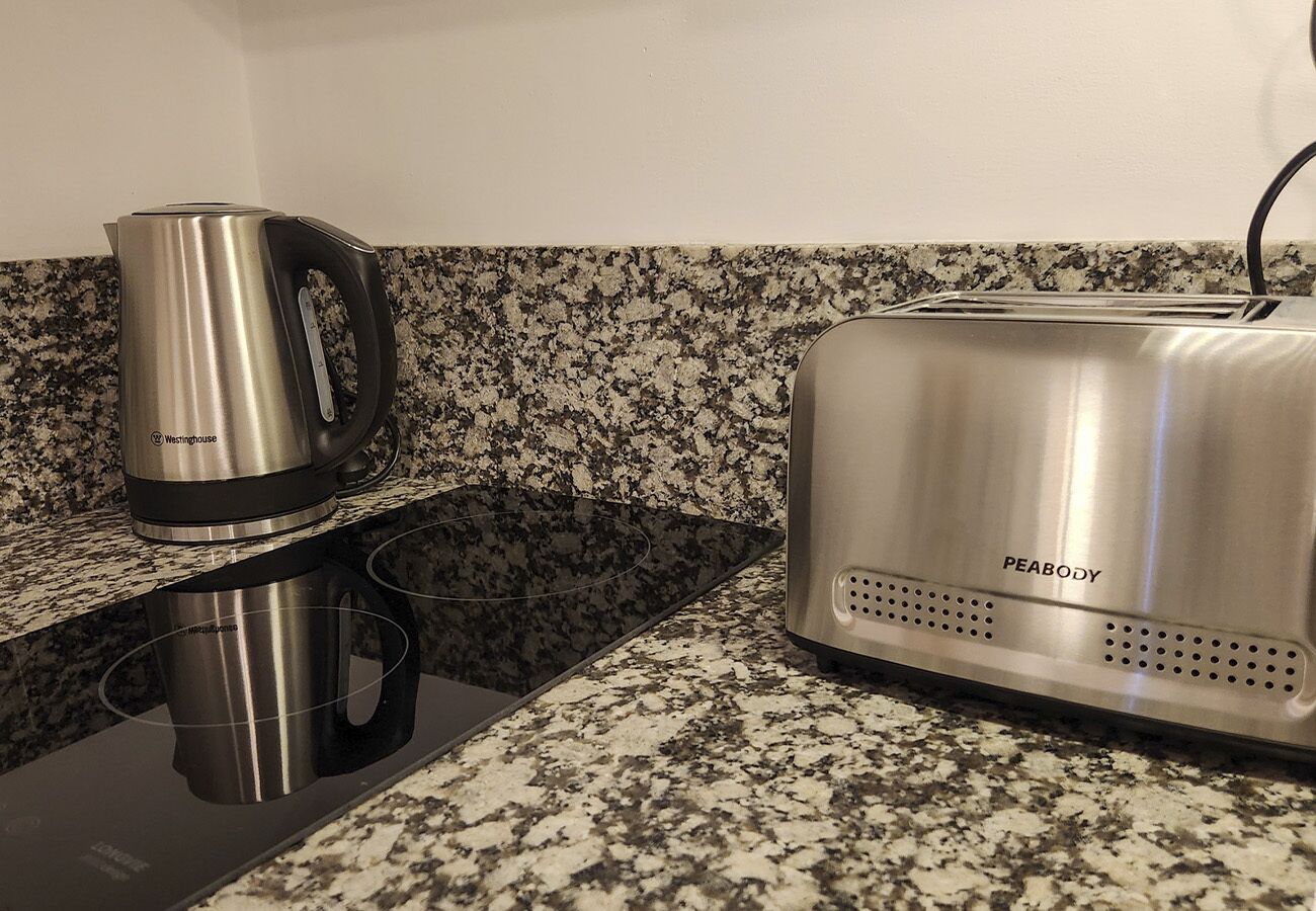 Uma cozinha com bancada de granito, chaleira de aço inoxidável e torradeira.