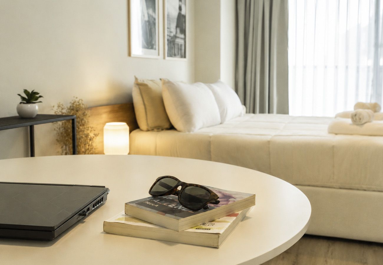 A modern bedroom with a bed, a bedside table with a lamp, and a laptop on a round table.