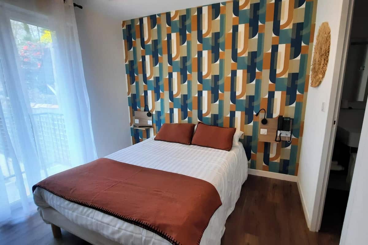 A bedroom with a patterned wall, a bed with a brown blanket, and a phone on the wall.
