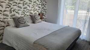 Una cama con una colcha blanca, dos almohadas con el texto 'PER ROS' y un plaid gris.