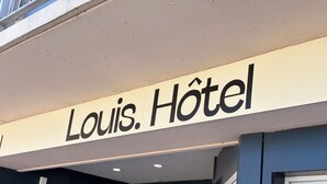 Un letrero de hotel con el nombre 'Louis. Hôtel' en letras grandes y negritas.