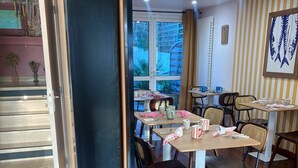 Un comedor con mesas y sillas de madera, vistas al exterior a través de grandes ventanales y una pared a rayas con un cuadro enmarcado.