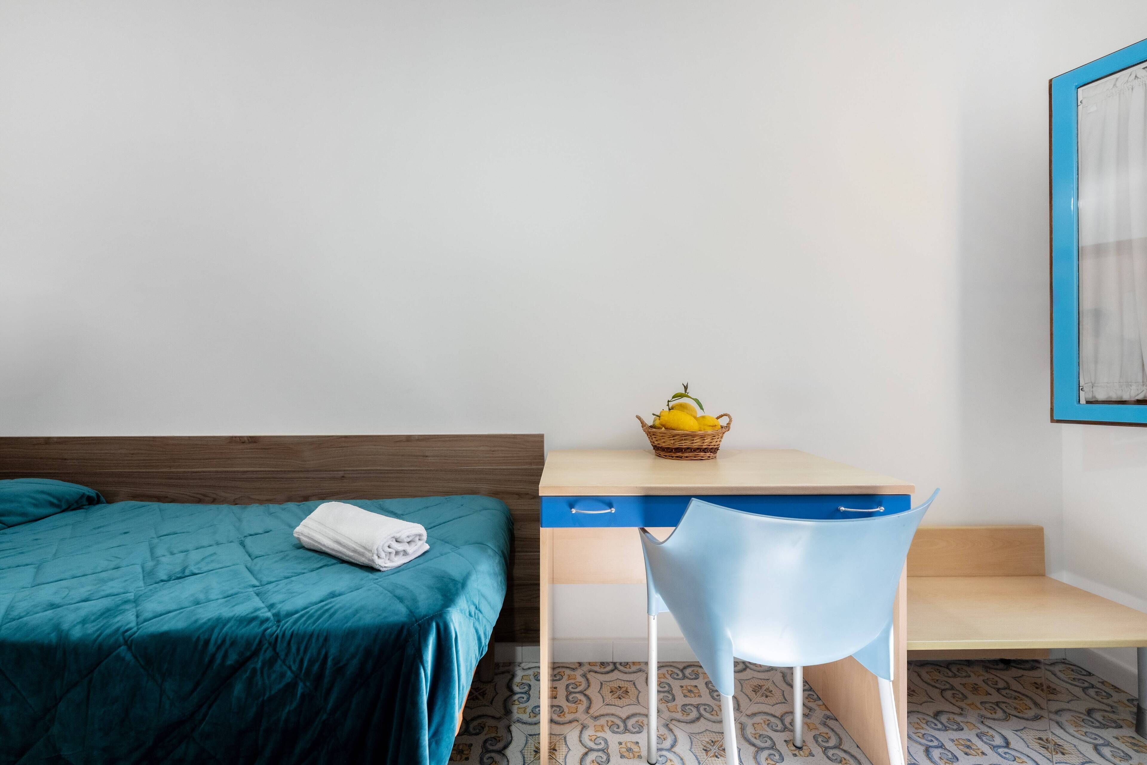 Una habitación con cama, escritorio, silla y estante en la pared.