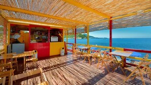 Un espace extérieur aménagé avec des tables et des chaises, un comptoir pour commander à emporter et une vue sur la mer.