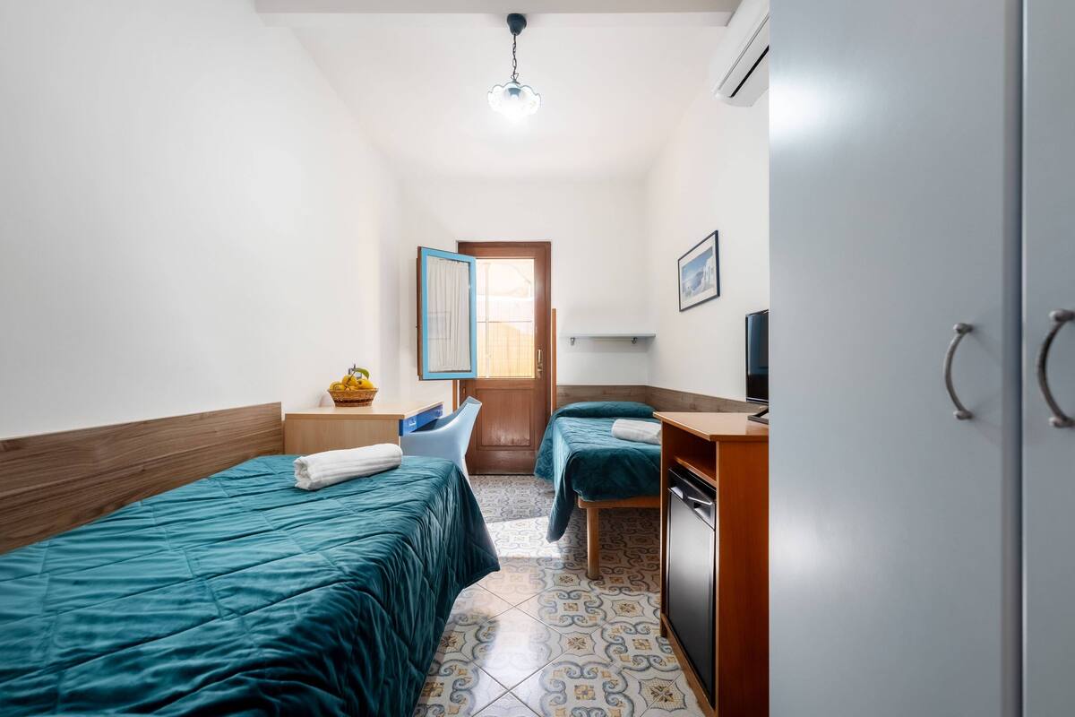 Un dormitorio con dos camas, un escritorio, una silla, un armario y una puerta que da a otra habitación.