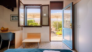 Une pièce comprenant un lit, un bureau, une chaise, une fenêtre avec des rideaux et une porte donnant sur un espace extérieur.