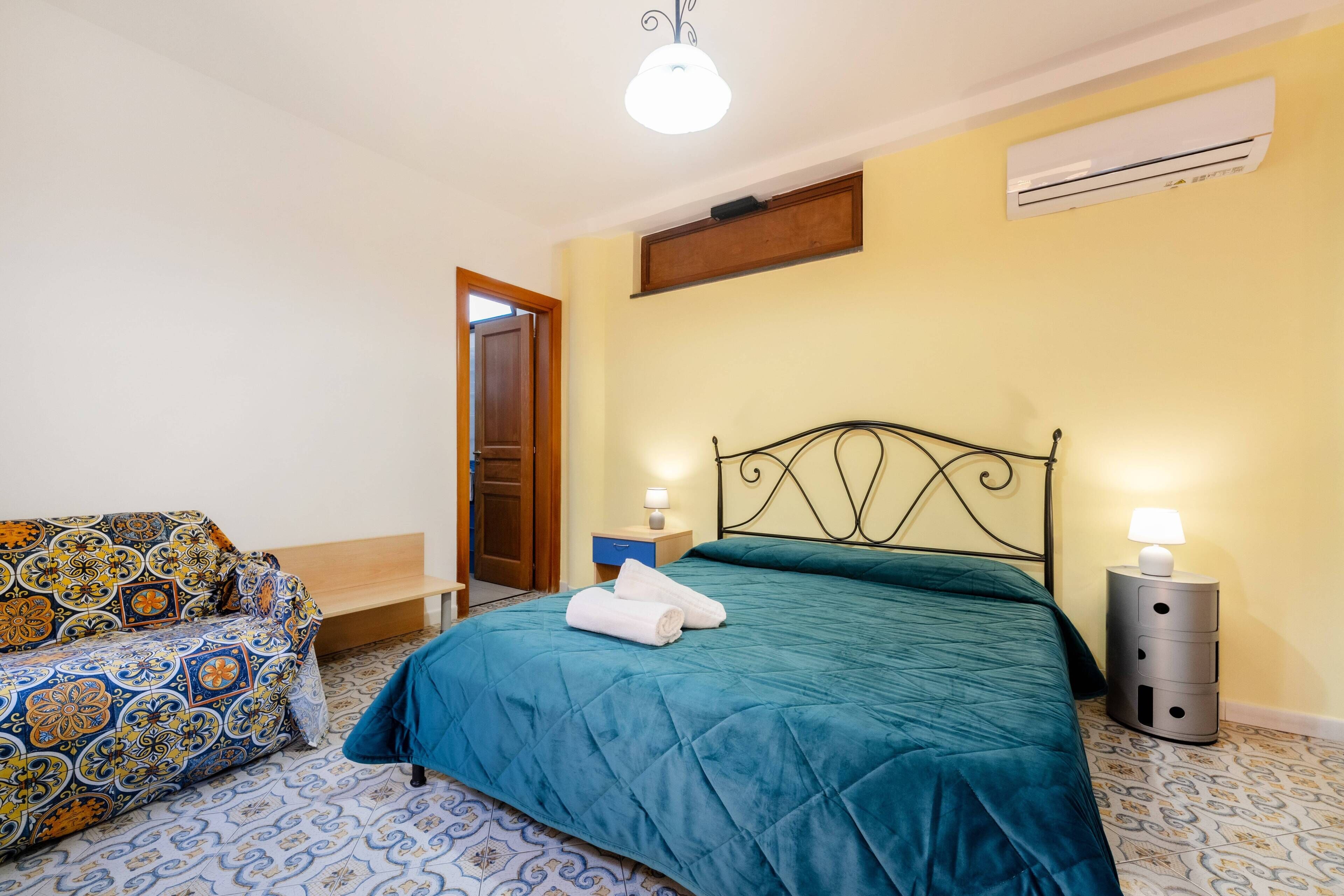 Un dormitorio con cama, mesita de noche, l ámpara y un sofá estampado.