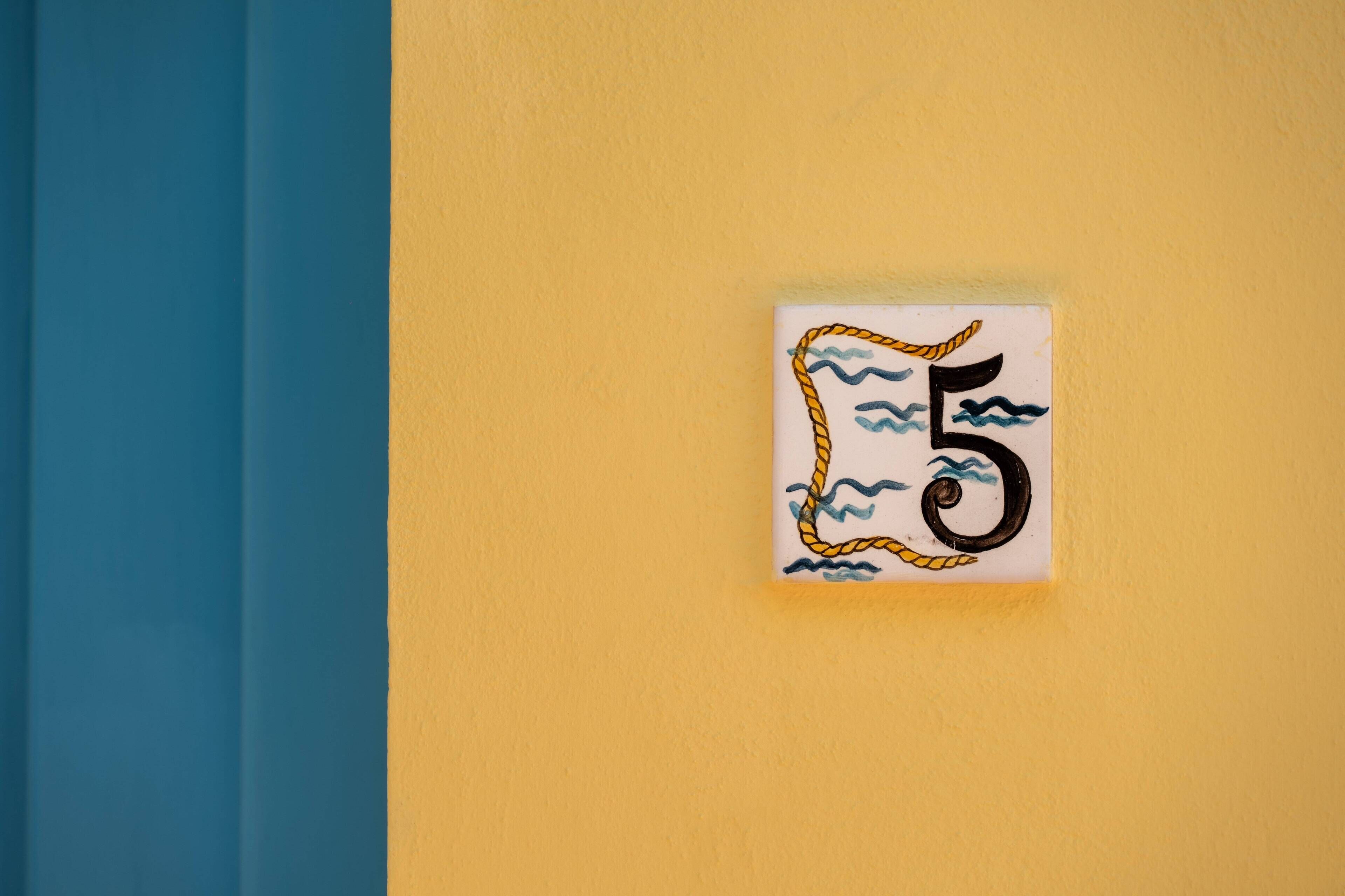 Una pared con un letrero del número 5, una pared azul y amarilla, y un pequeño letrero blanco con un diseño de cuerda y olas.