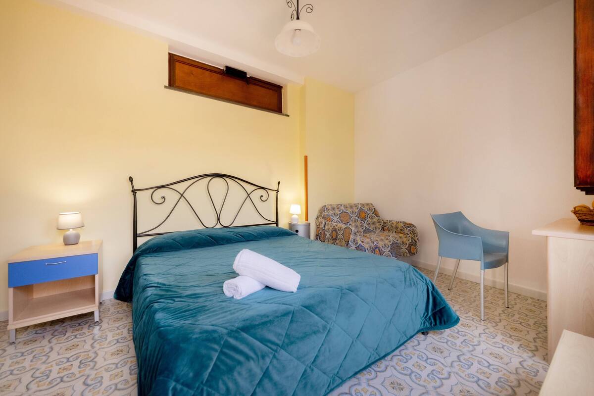 Un dormitorio con cama, mesita de noche, silla y escritorio.