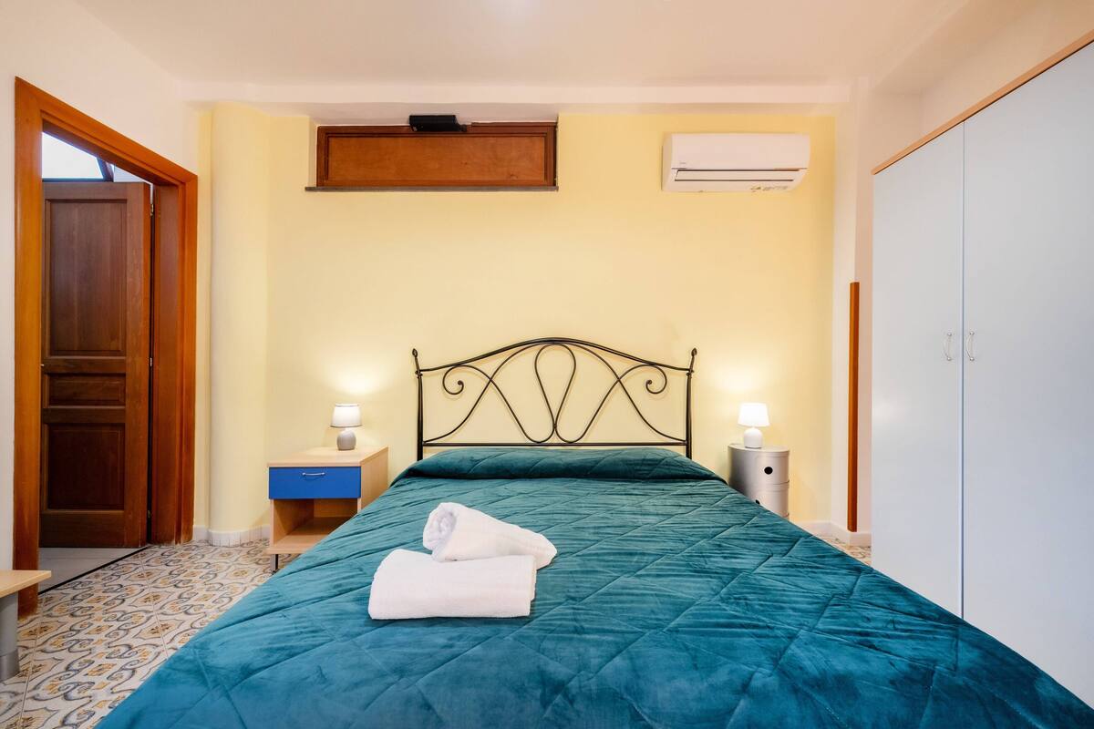 Un dormitorio con cama, mesita de noche, armario, puerta y unidad de aire acondicionado.