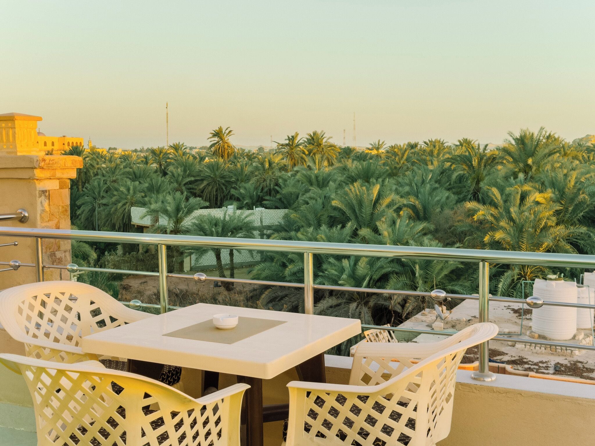 Un balcón con mesa y sillas, con vista a un jardín de palmeras.