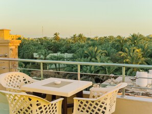 A balcony with a table and chairs, overlooking a palm tree garden. - Nigmt Siwa Hotel (Siwa)