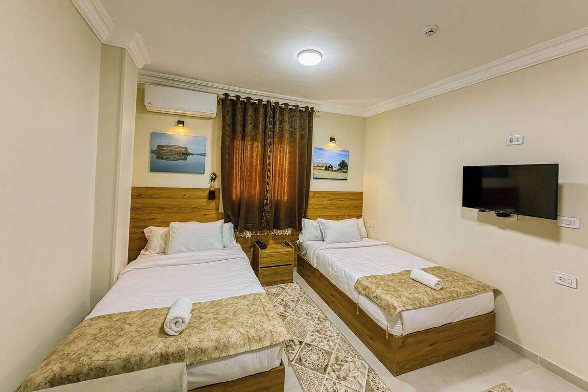 A hotel room with two beds, a TV, and artwork on the walls.