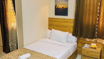 Habitación de hotel con cama, mesita de noche, equipo de aire acondicionado, un cuadro y cortinas.
