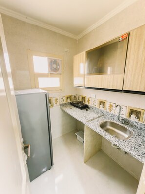A compact kitchen with a refrigerator, granite countertop, sink, and a window with a fan. - Nigmt Siwa Hotel (Siwa)