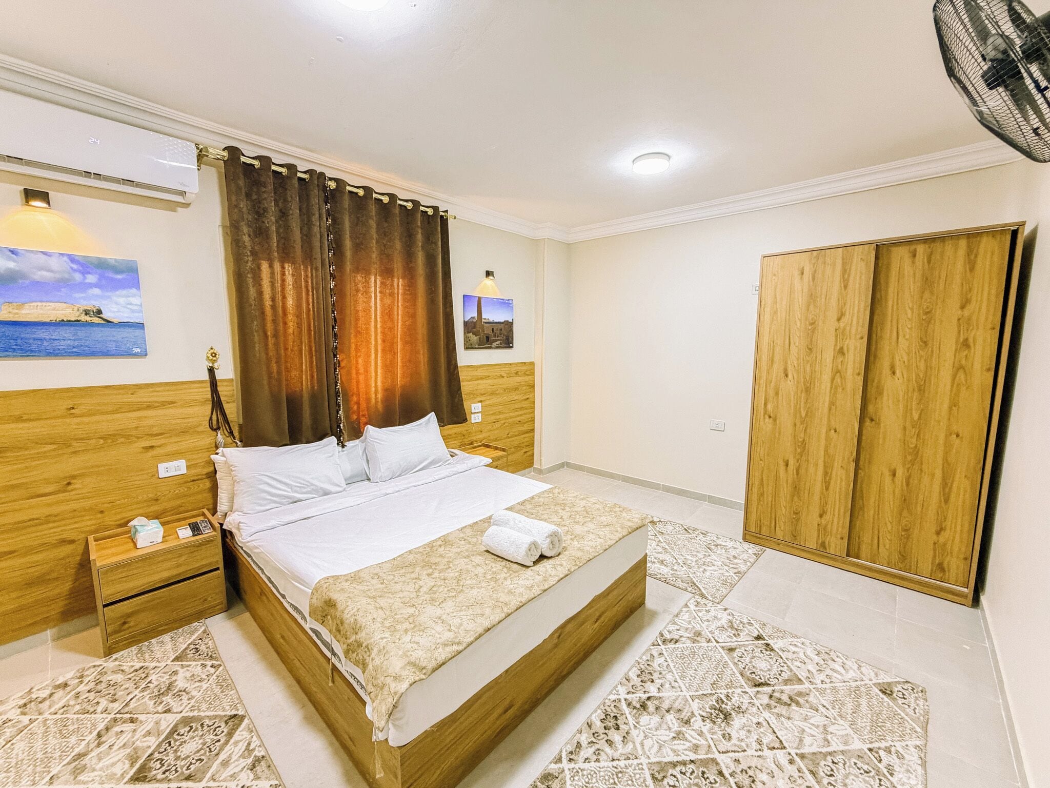 Una camera da letto con un letto, comodini, un armadio in legno, una ventola a soffitto e opere d'arte alle pareti.