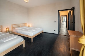 A hotel room with two beds, wooden headboards, a dark wooden floor, a wooden dresser, and a hallway leading to another room. - Grand Central Station Two Bedroom Apartment (Antwerp)