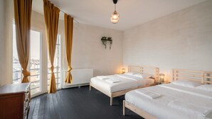 Ein Hotelzimmer mit zwei Betten, einem Holztisch, einer Heizung und Blick auf die Stadt durch große Fenster.