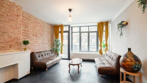 Ein Wohnzimmer mit Ziegelwand, zwei Sofas, einem Couchtisch und einer großen Vase.