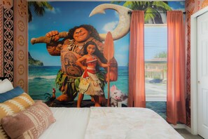 Ein Schlafzimmer mit einer Wandmalerei einer tropischen Szene, einem Bett mit gemusterten Kissen und einem Fenster mit Vorhängen.